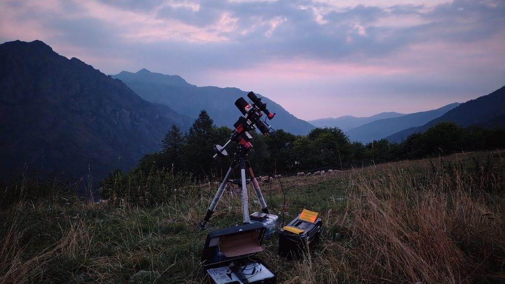 Telescopio astronomico su montatura equatoriale in montagna al tramonto, pronto per una sessione di astrofotografia.